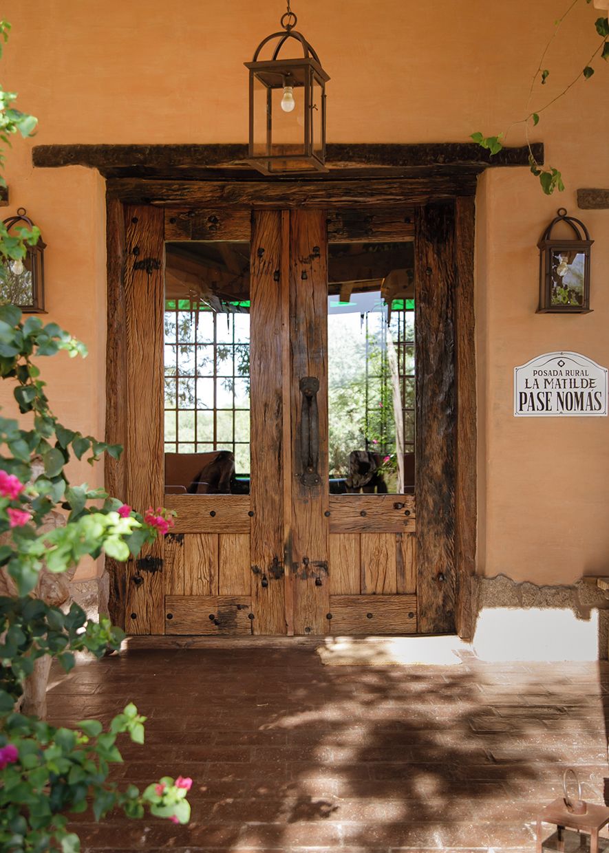 A rustic wooden door with a lantern above it, leading to a room with a view of greenery outside.