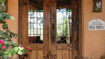 A rustic wooden door with a lantern above it, leading to a room with a view of greenery outside.