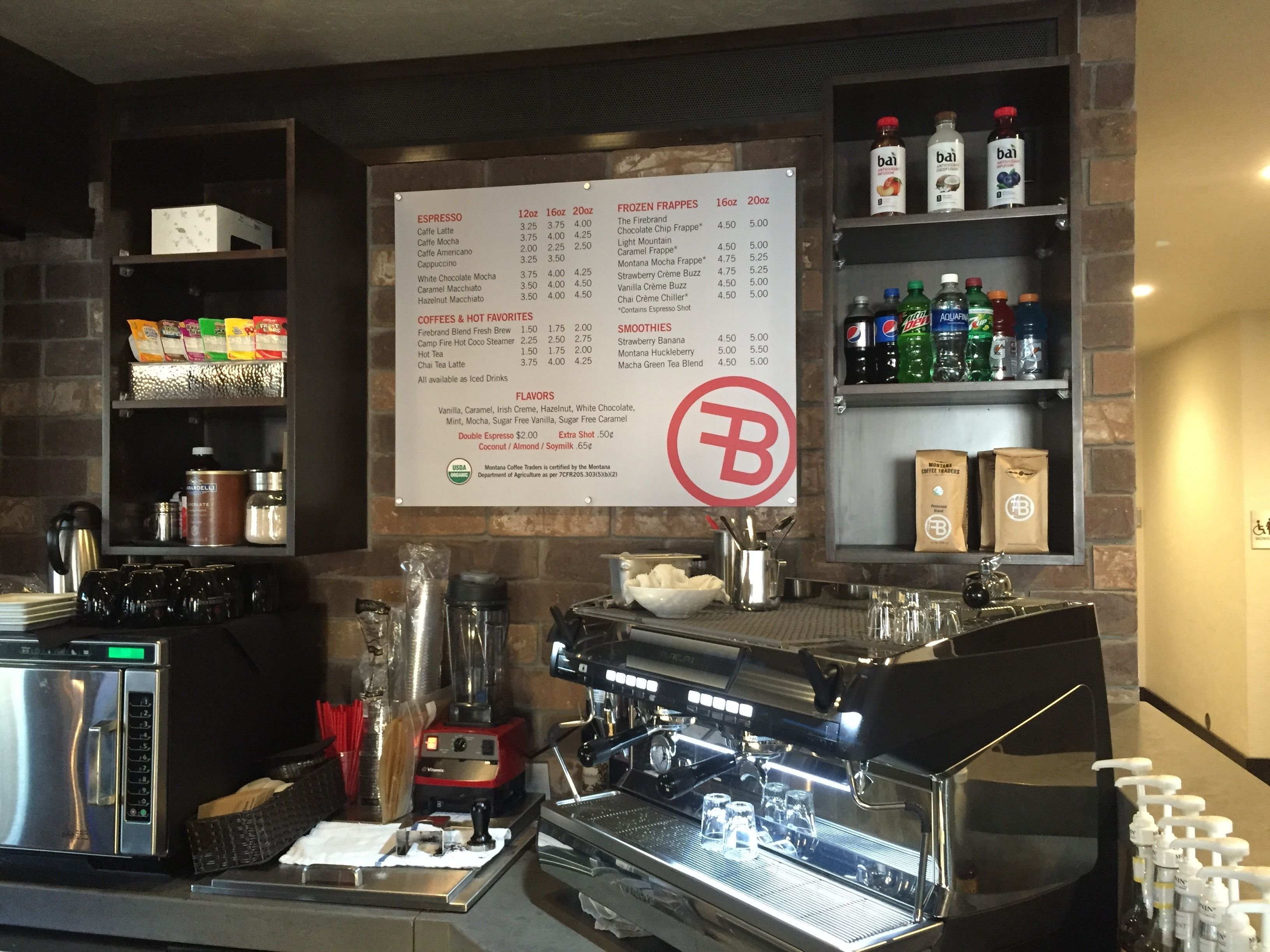 Interieur van een koffiebar met een menubord, espresso machines en diverse koffieproducten op planken.