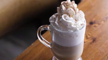 A clear glass mug with a handle, filled with a layered beverage and topped with whipped cream and a sprinkle of cocoa powder.