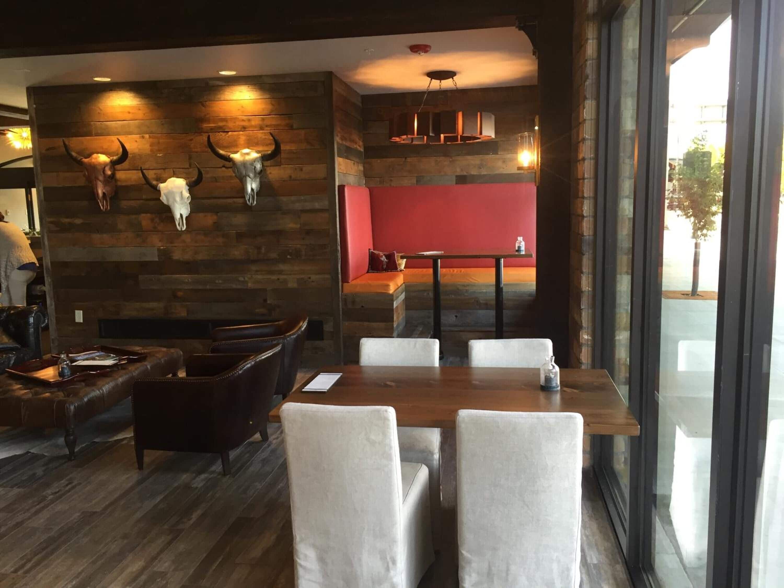 A restaurant interior with a wooden wall, a red accent wall, and a dining area with a table and chairs.