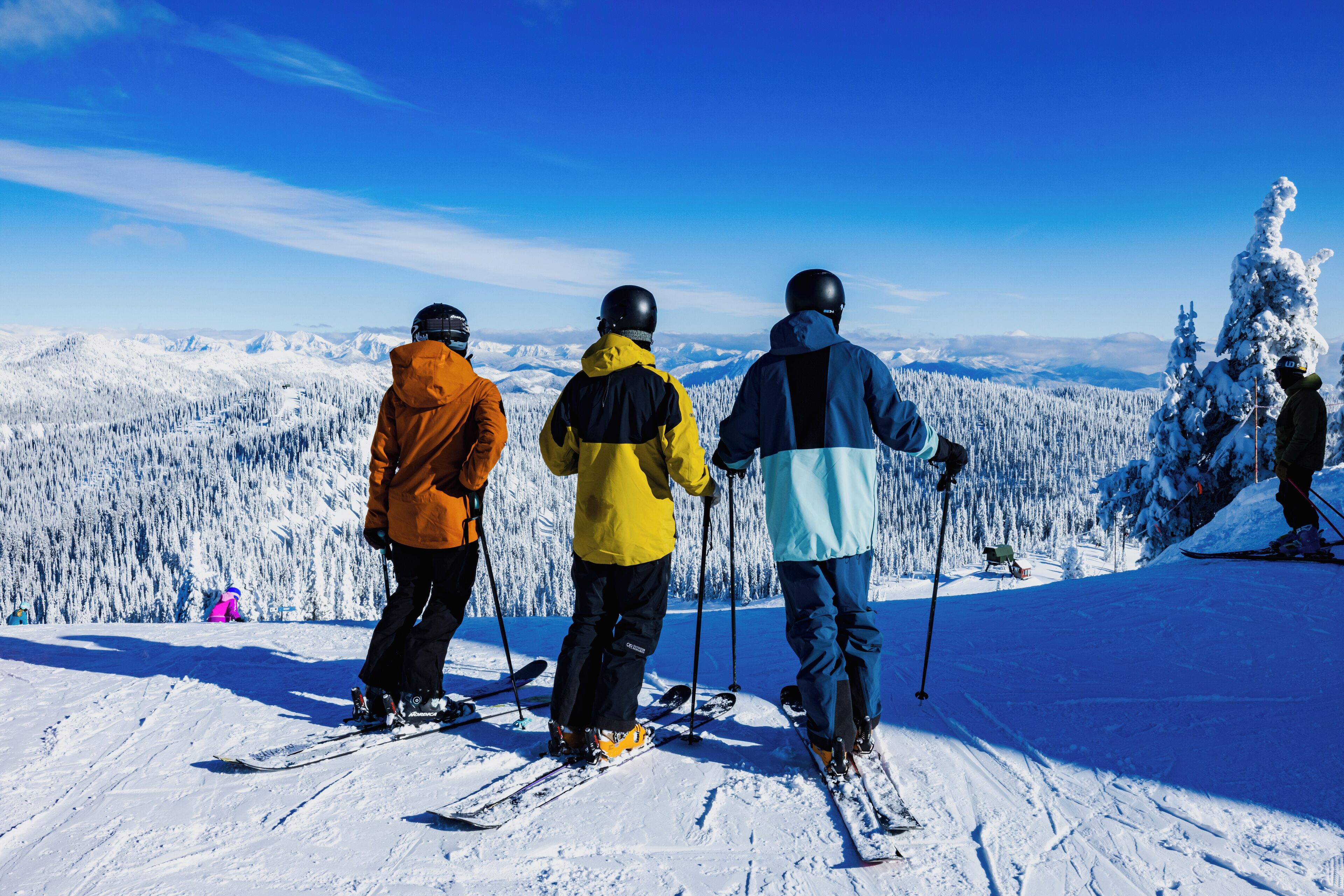 Three skiers on a snowy mountain with a clear sky.