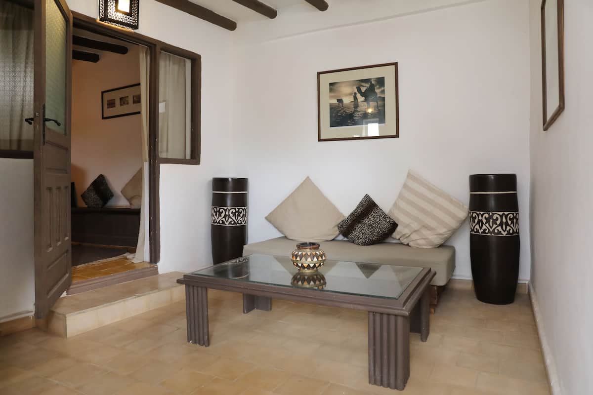 A living room with a glass coffee table, a sofa with patterned cushions, and two tall vases.