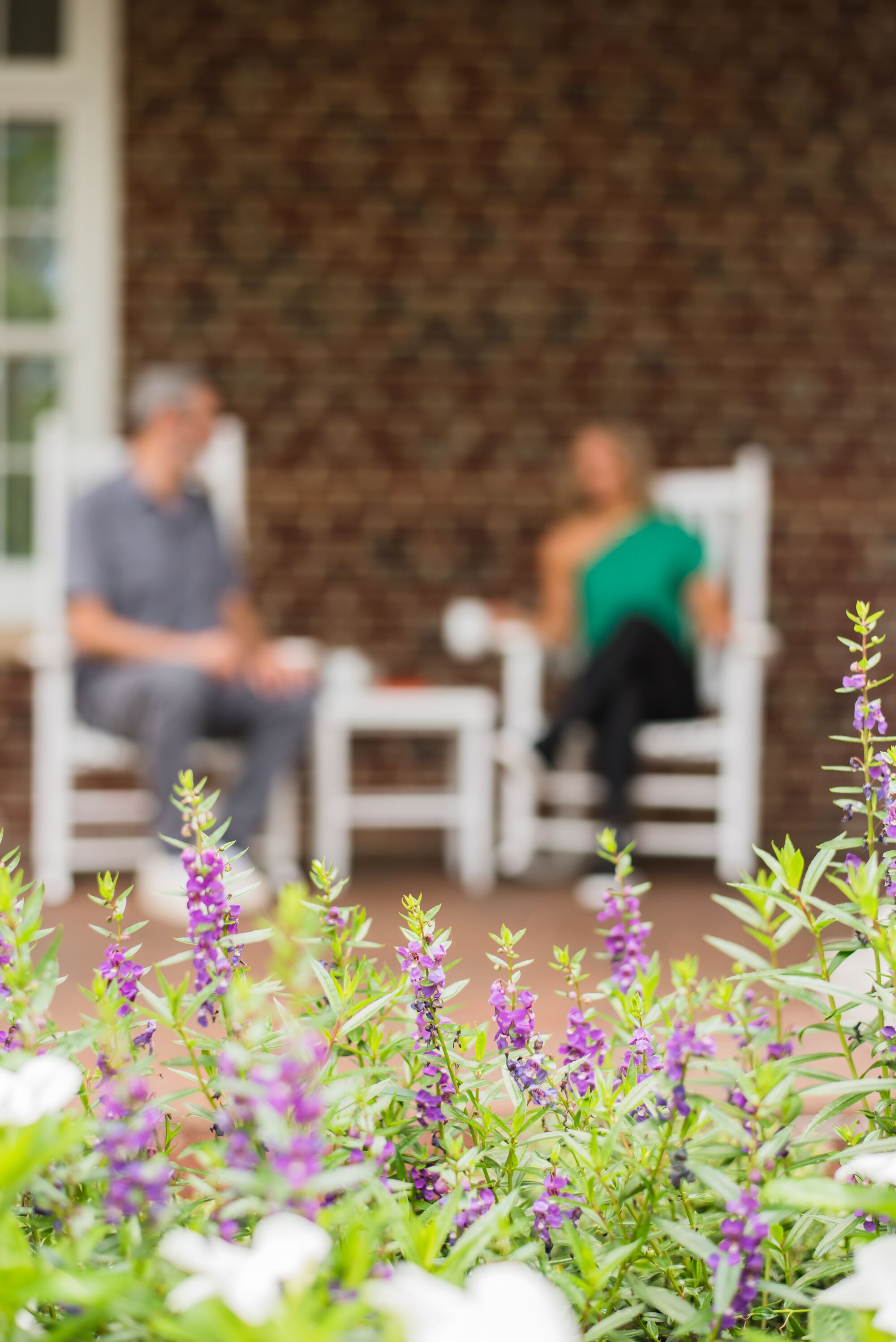 A patio area with two white chairs, a table, and purple flowers in the foreground.