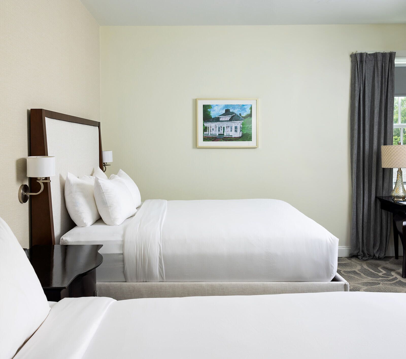 A hotel room with a bed, a nightstand, a lamp, a painting, and a window with curtains.
