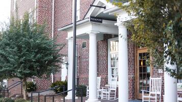 A brick building with a covered entrance, white columns, and outdoor seating.