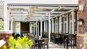 An outdoor patio with tables and chairs, a white pergola, and brick walls. - The Mayton (Cary)