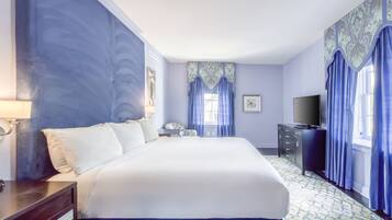 Una habitación de hotel con una cama grande, un aparador, un televisor y una ventana con cortinas azules.