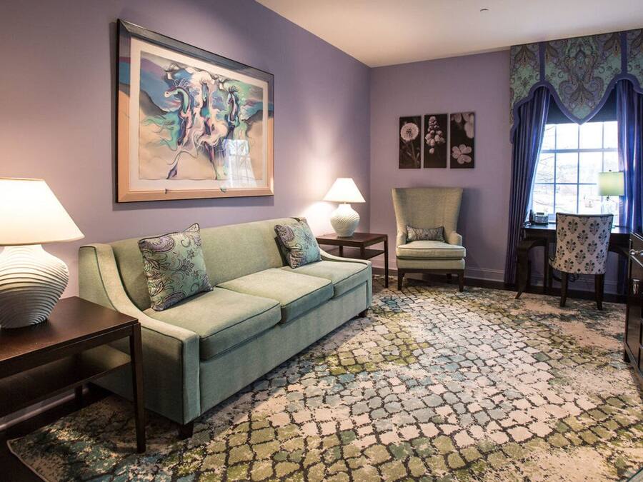 A room with a green sofa, two side tables with lamps, a patterned rug, a chair, and a large painting on the wall.