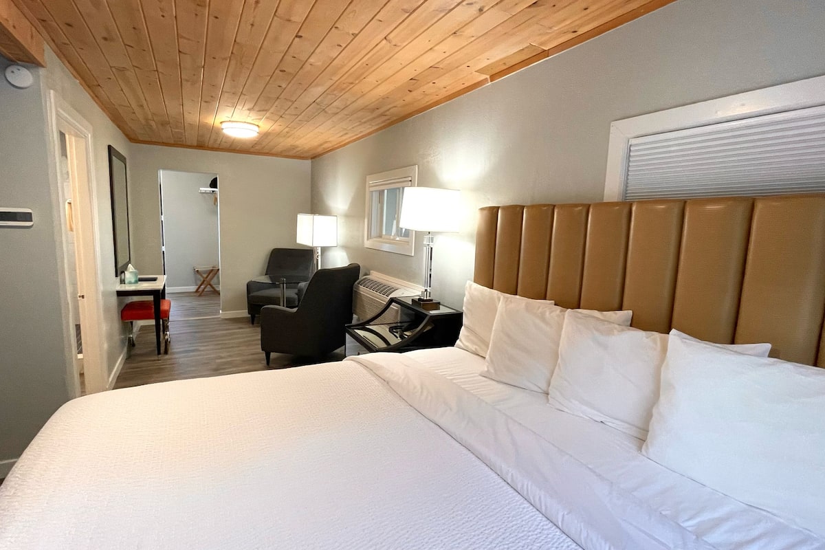 Una habitación de hotel con una cama grande, un escritorio con silla, una mesita pequeña y una lámpara.