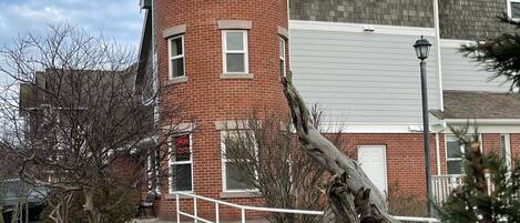 Un bâtiment en briques avec un coin arrondi, une balustrade blanche et un grand arbre au premier plan.