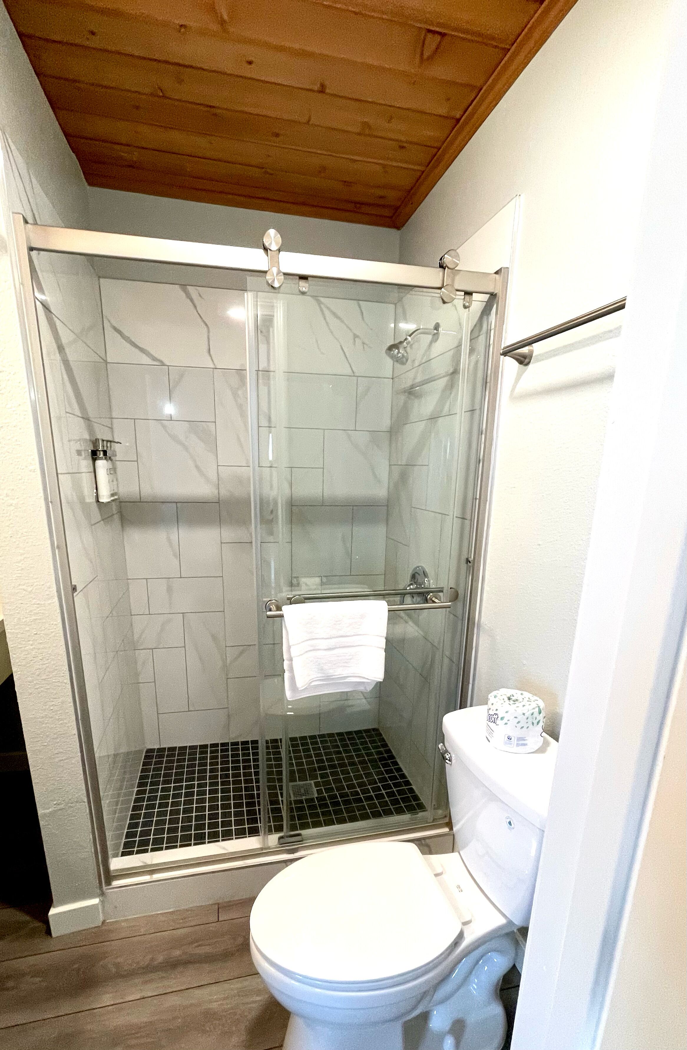A bathroom with a glass-enclosed shower, a white toilet, and a tiled floor.