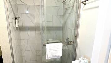 A bathroom with a glass-enclosed shower, a white toilet, and a tiled floor.