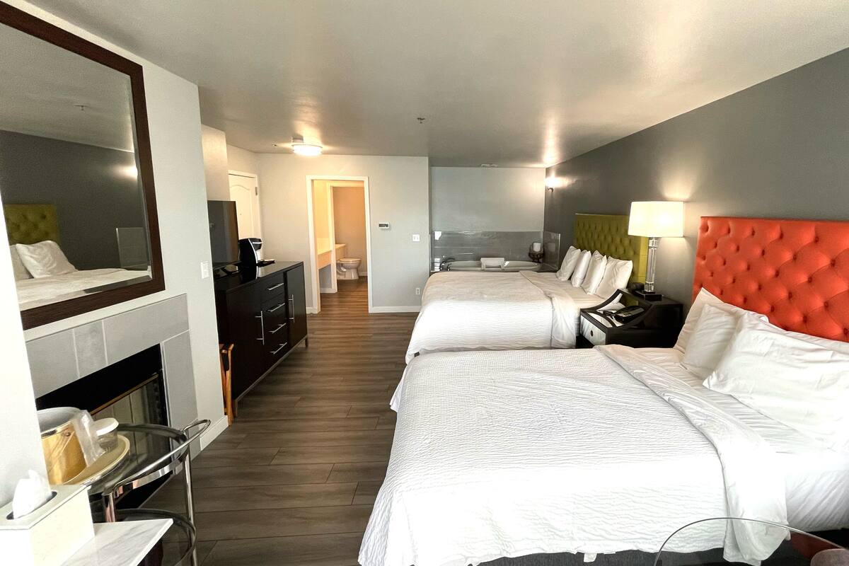 Una habitación de hotel con dos camas, un baño, un espejo y un pequeño rincón de descanso.
