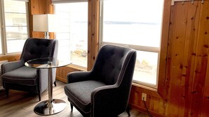 A room with two black armchairs, a small glass table, and a view of the outdoors through large windows. - Tides Inn & Suites (Port Townsend)