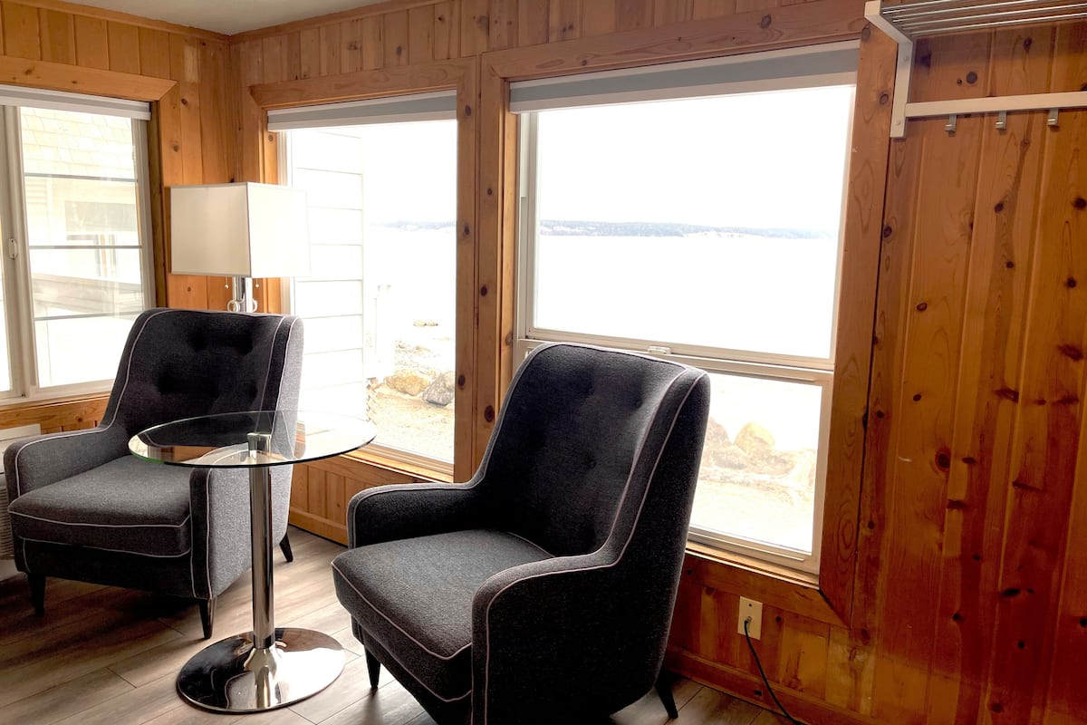 Una habitación con dos sillones negros, una mesita de cristal y vistas al exterior a través de amplios ventanales.