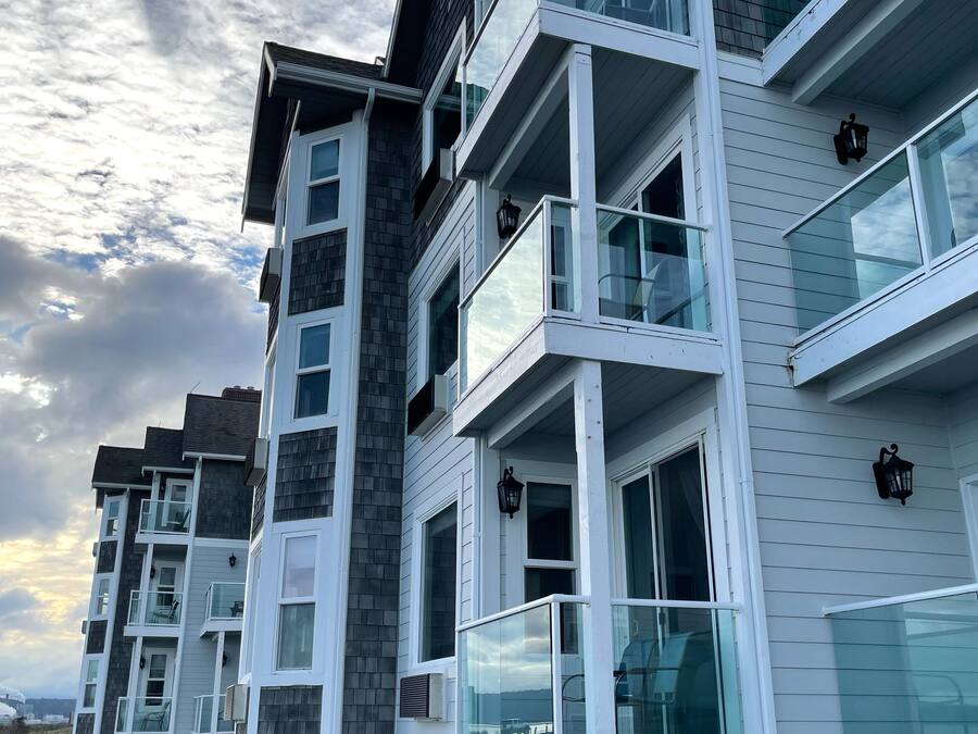A multi-story residential building with balconies, large windows, and a gravel driveway.