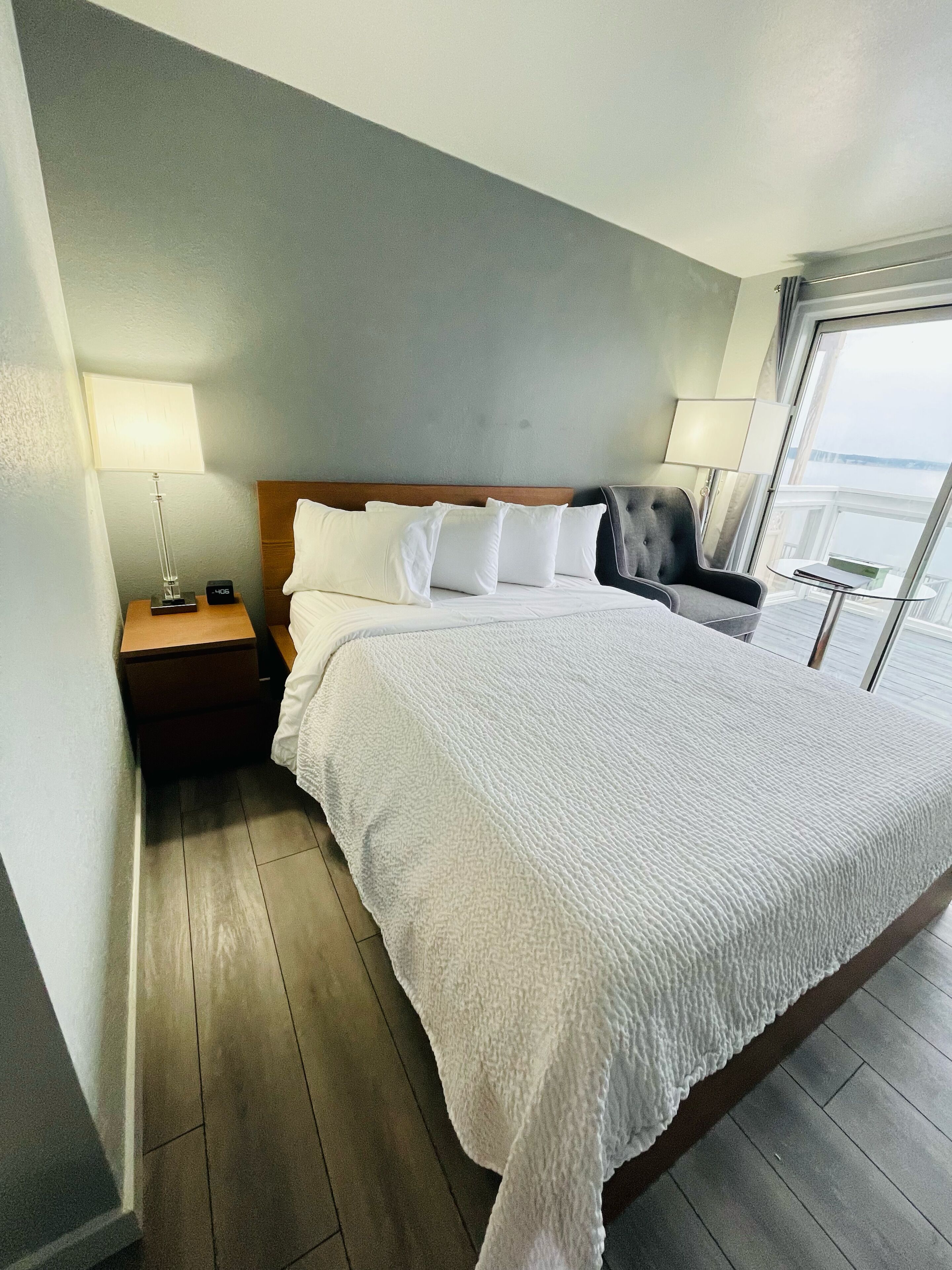 A neatly made bed with white linens, a wooden headboard, and a nightstand with a lamp and a clock.