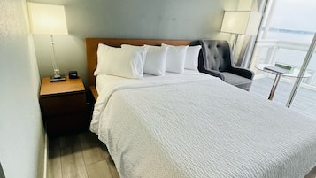 A neatly made bed with white linens, a wooden headboard, and a nightstand with a lamp and a clock.