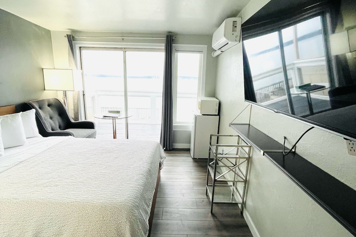Habitación de hotel con cama, una silla, una mesita, aire acondicionado y ventana con vistas.