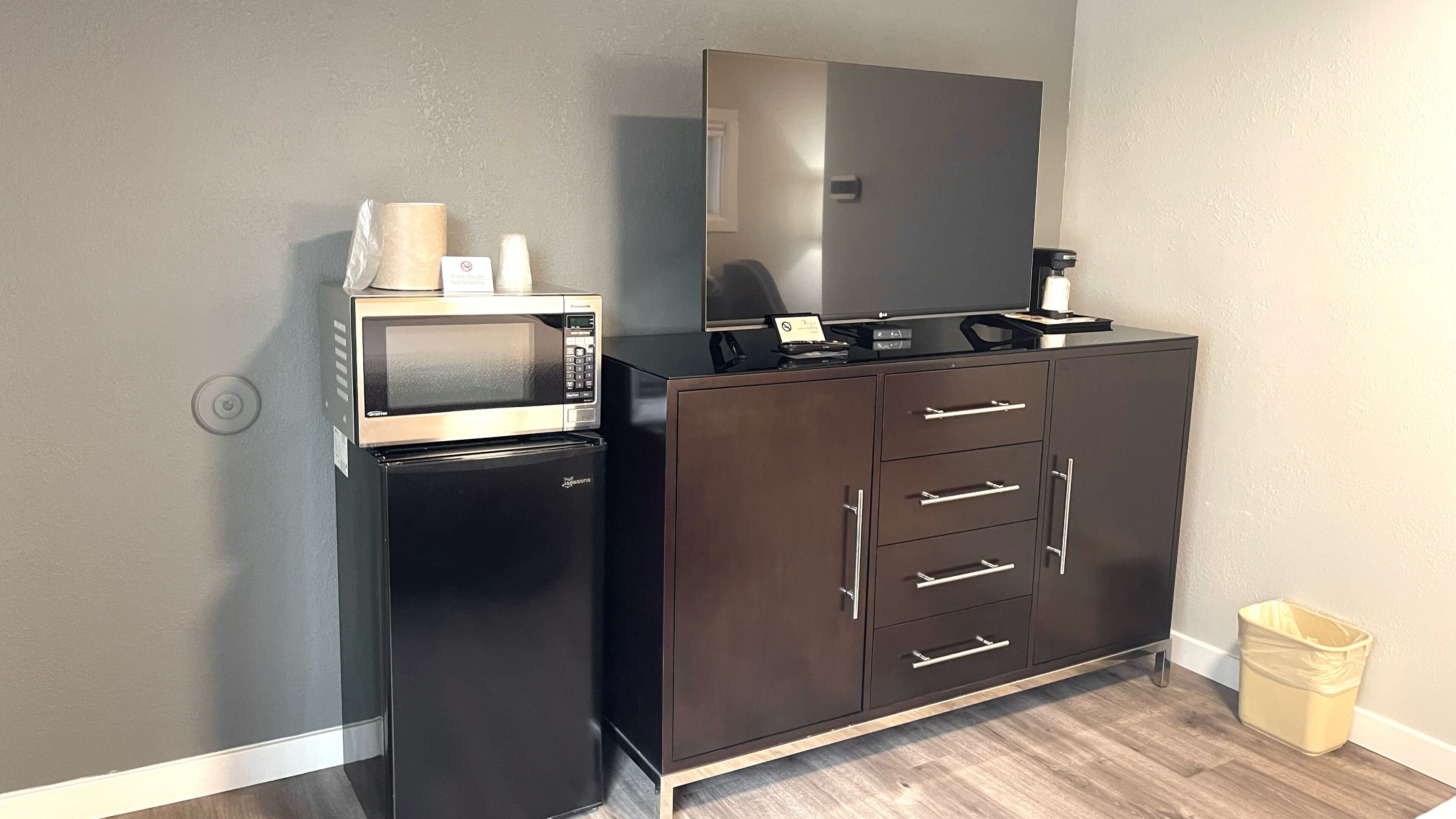 Una kitchenette con microondas, refrigerador y un mueble oscuro con cajones.