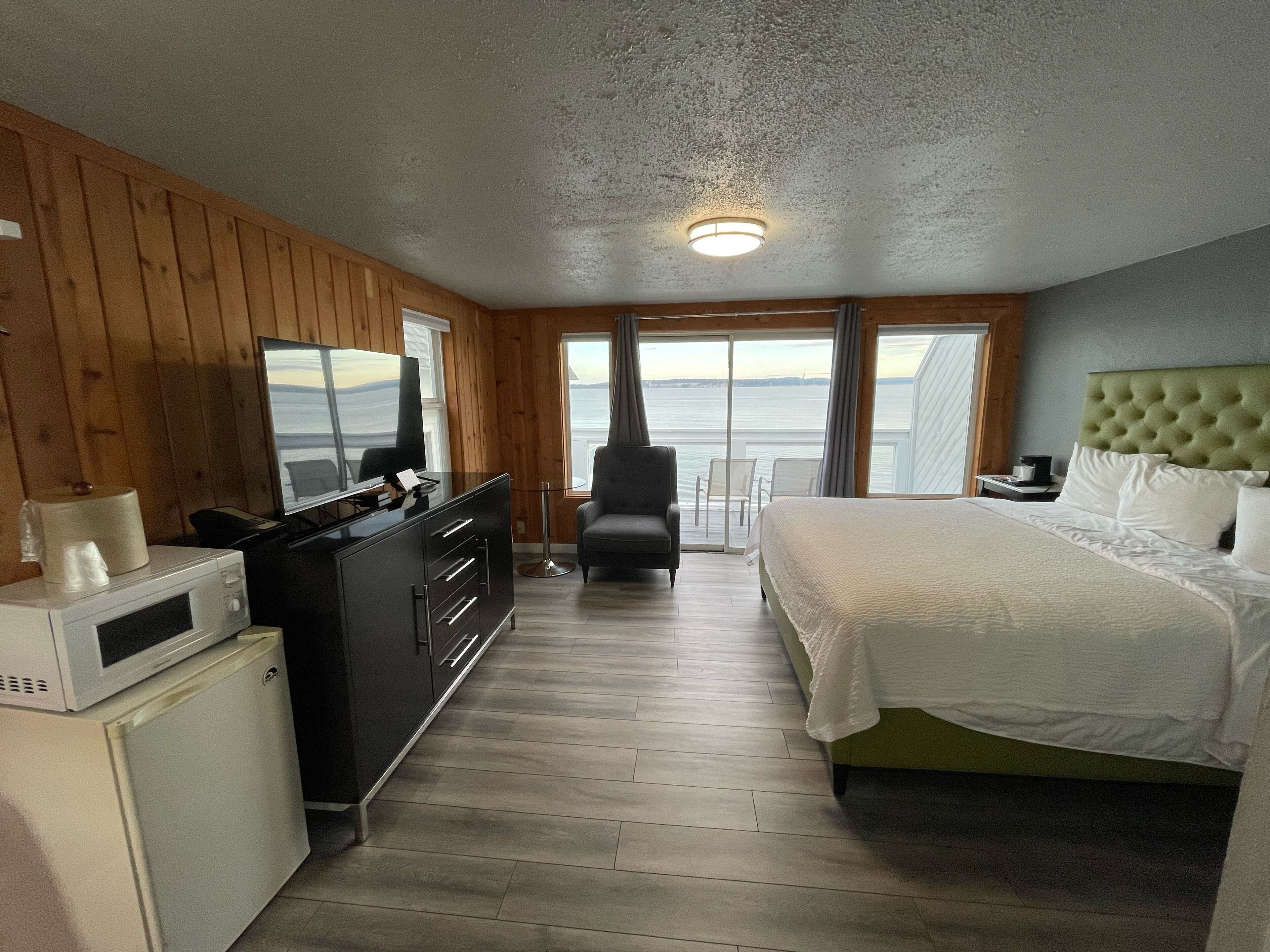 A room with a bed, a desk, a chair, a television, and a view of the sea.