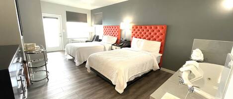 Habitación de hotel con dos camas, un escritorio, una silla, un tocador con espejo y un baño con lavamanos e inodoro.