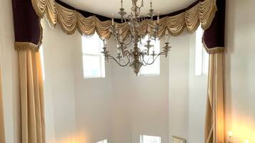 A room with a large window, a chandelier, and a white bench.