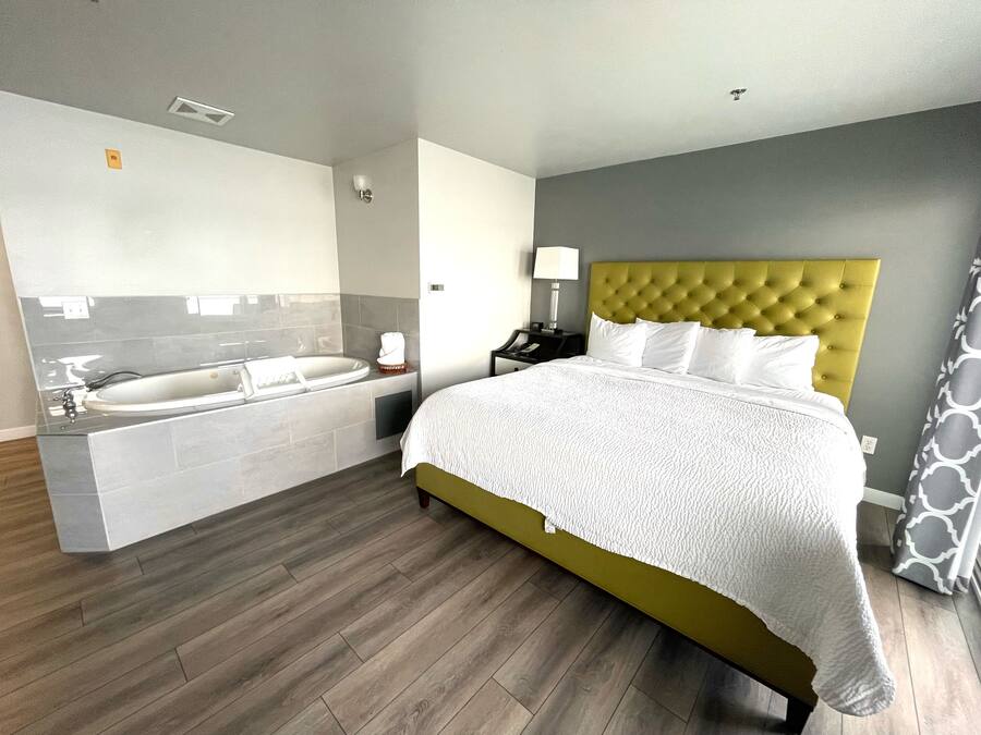 A hotel room with a bed, a bathroom with a bathtub, and a nightstand with a lamp.
