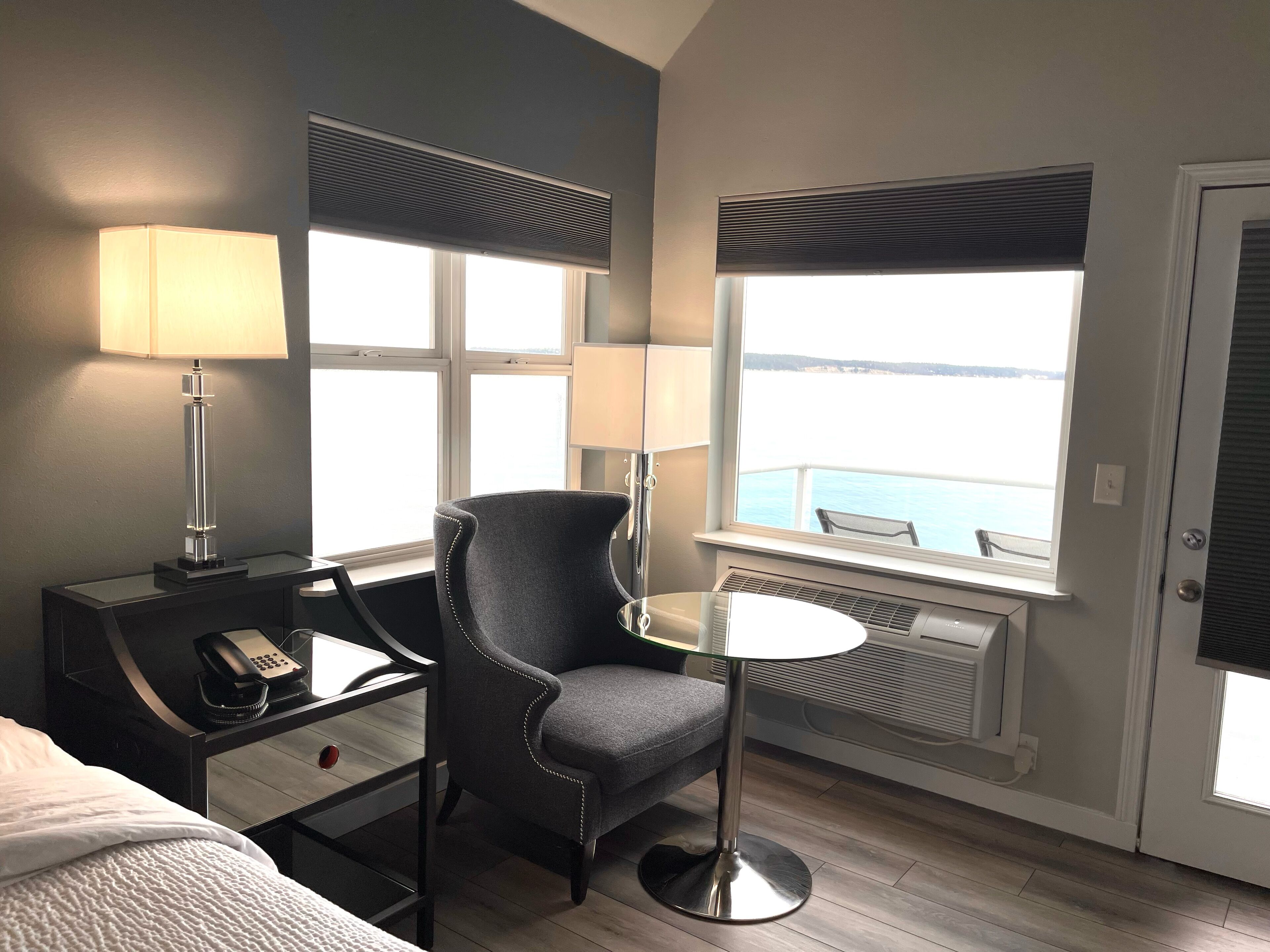 Ein Hotelzimmer mit Bett, Schreibtisch mit Telefon, Stuhl, Tisch mit Lampe und Fenster mit Meerblick.