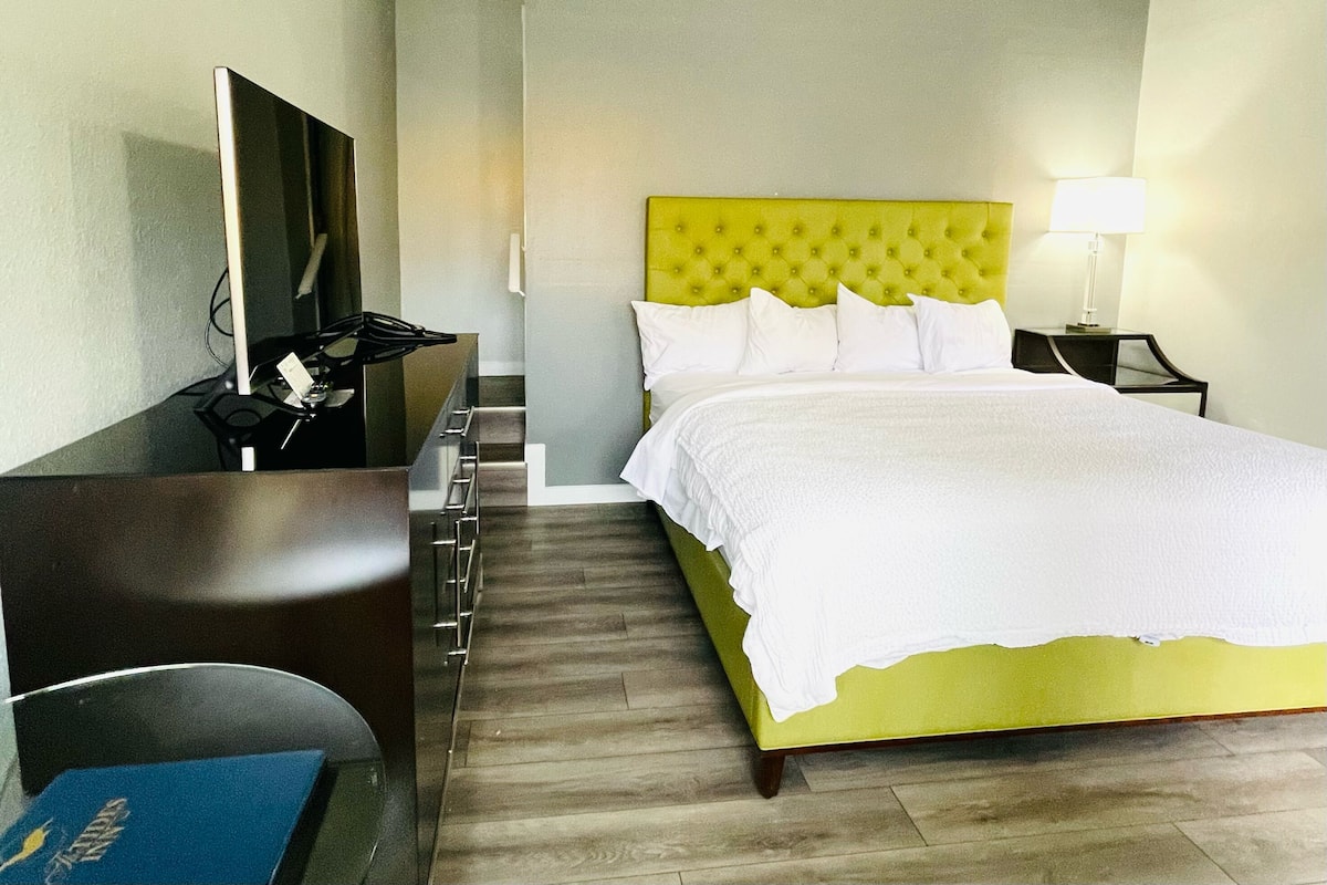 Una habitación de hotel con una cama, un escritorio con una silla, una lámpara y un televisor.