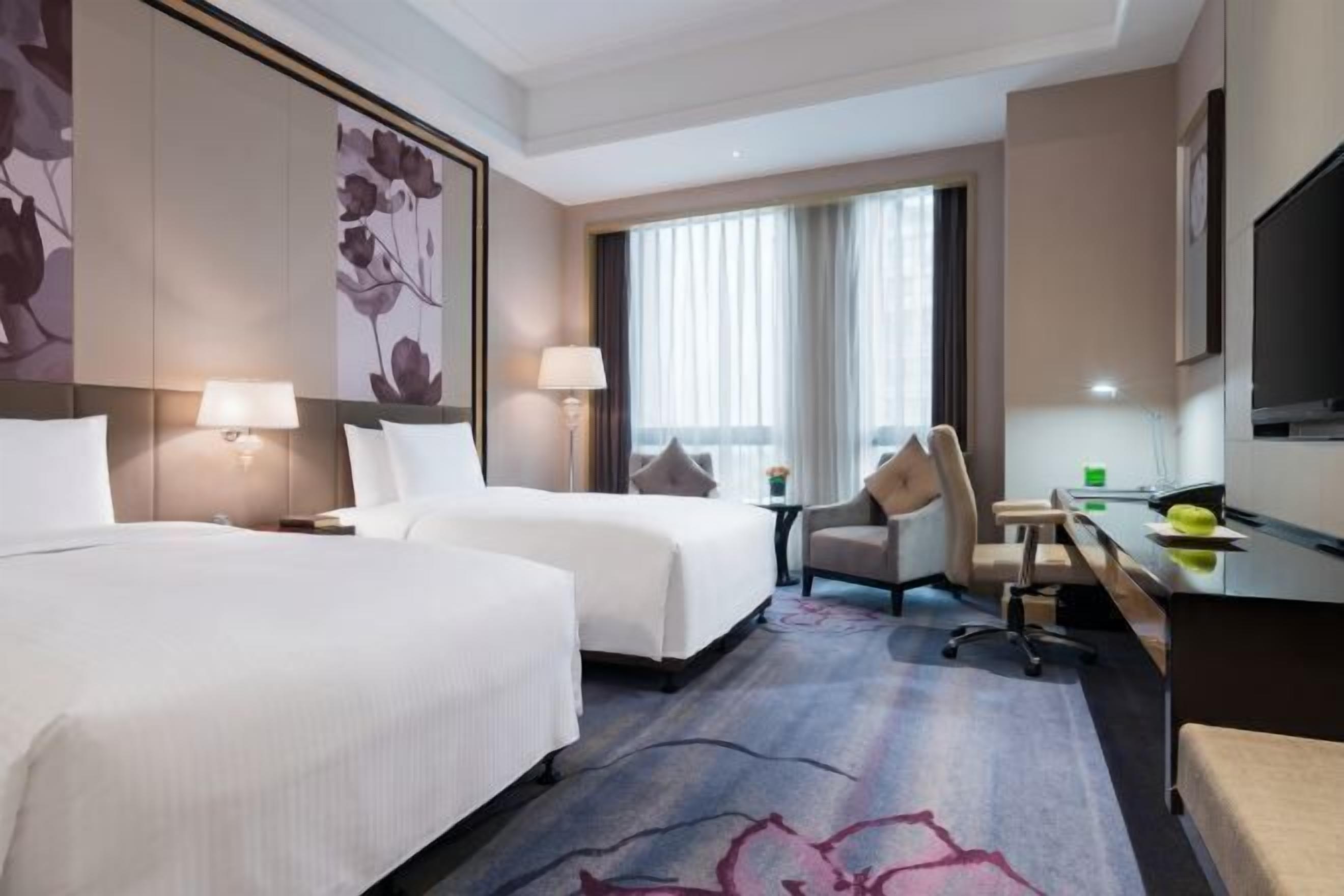 Une chambre d’hôtel avec deux lits, un bureau, une chaise, une télévision et une grande fenêtre.