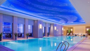 A modern indoor swimming pool with a blue-lit ceiling, clear pool water, and lounge chairs along the poolside. - Wanda Realm Zengcheng Guangzhou (GUANGZHOU)