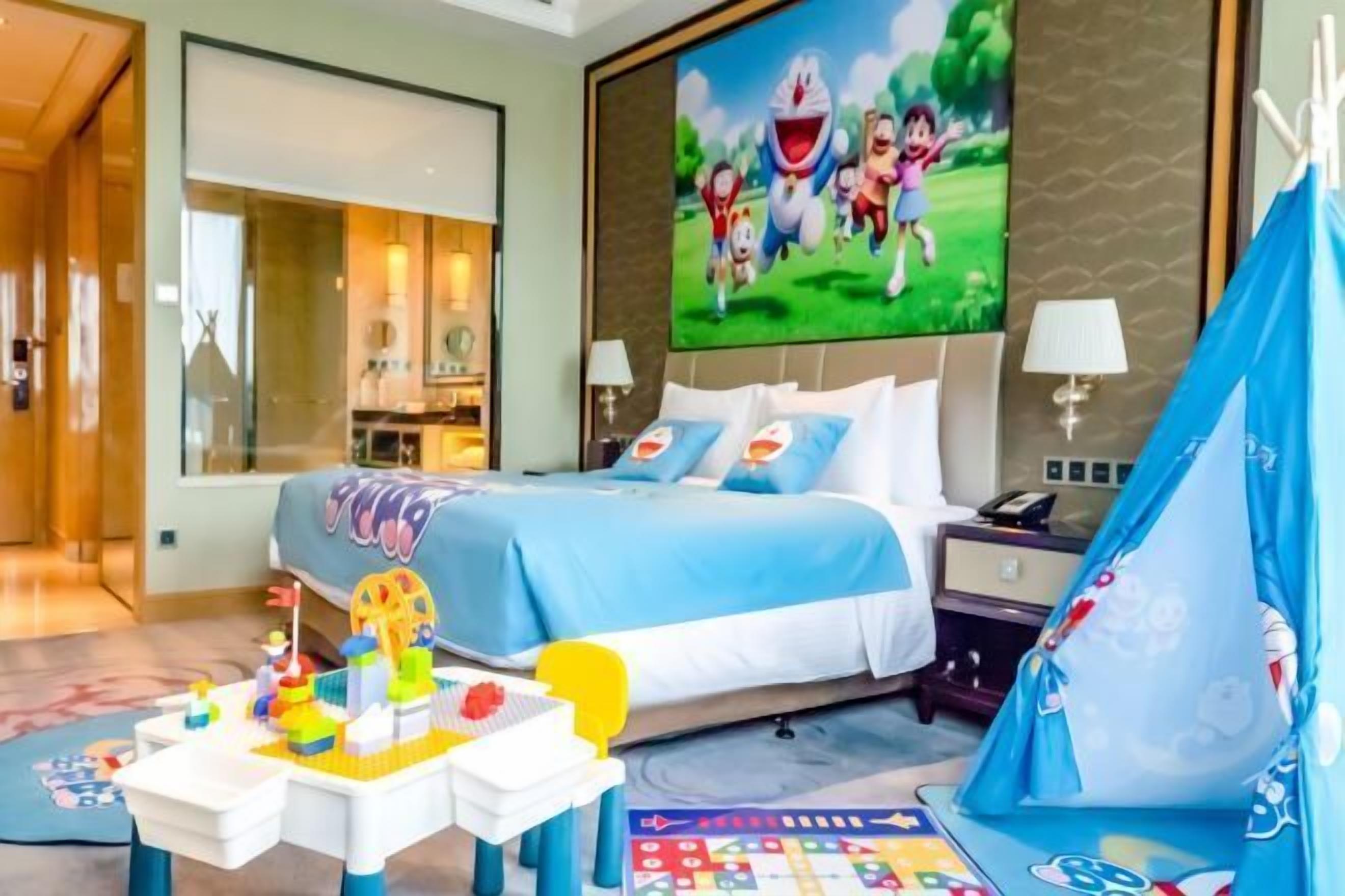 Une chambre d’hôtel avec un lit, un bureau avec des jouets, une tente et un grand écran de télévision.