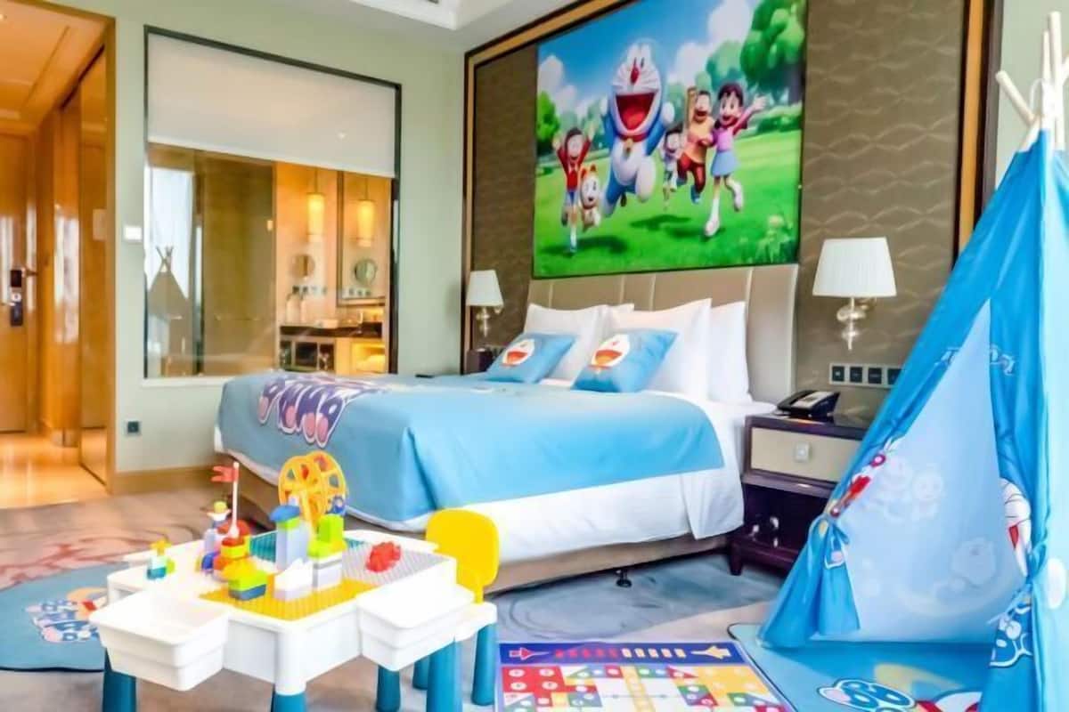 A hotel room with a bed, a desk with toys, a tent, and a large TV screen.