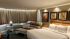 A hotel room with a large bed, a desk with a lamp, a chair, and a wall with framed artwork.
