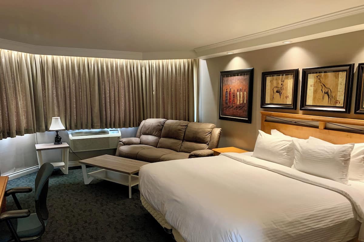 Habitación de hotel con una cama grande, un escritorio con lámpara, una silla y una pared decorada con cuadros.