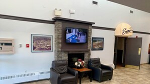 A lobby with a fireplace, two leather armchairs, a television mounted above it, and framed pictures on the walls.