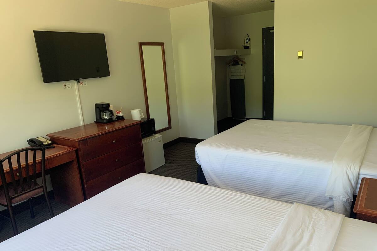 Habitación de hotel con dos camas, un escritorio, una silla, un televisor y un espejo.