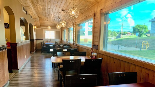 A restaurant with wooden interior, tables, chairs, and large windows offering a view of the outside.