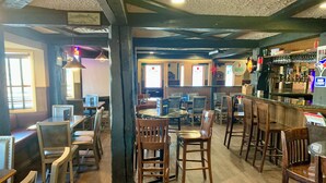 A restaurant with wooden tables and chairs, a bar area with a counter, and a view of the street through large windows.