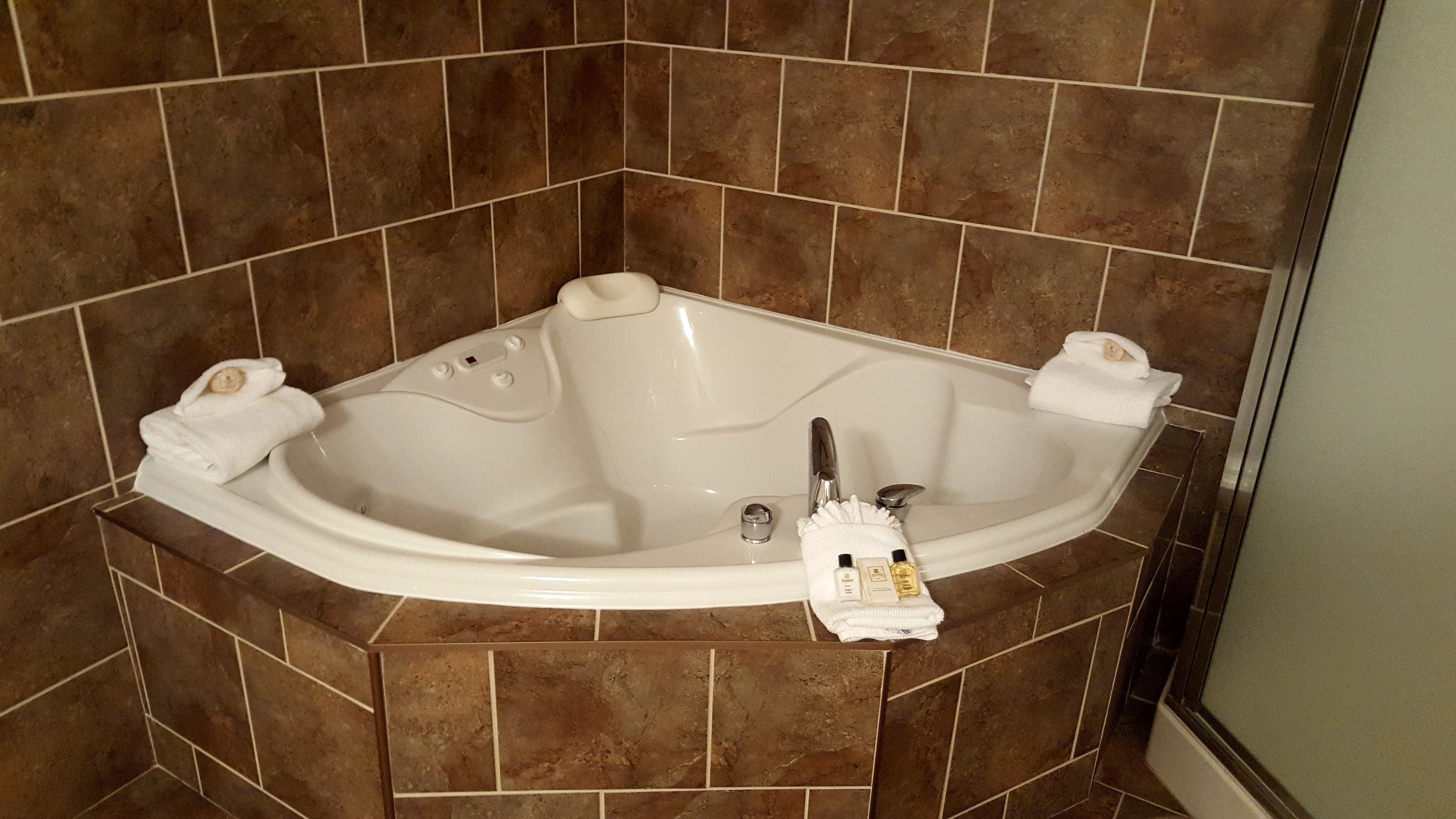 A corner bathtub with two towels, a bottle, and a plug.