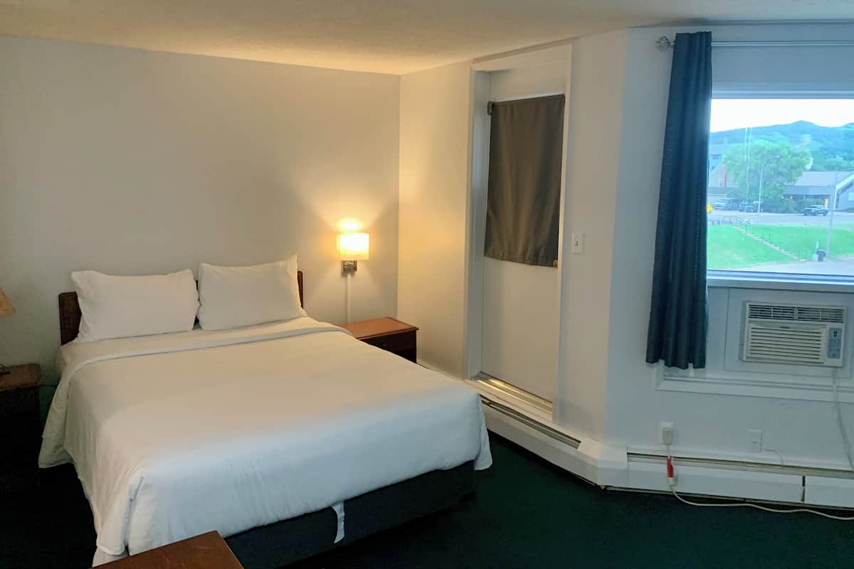 Habitación de hotel con cama, mesitas de noche, lámpara de pared, equipo de aire acondicionado y ventana con vistas al exterior.