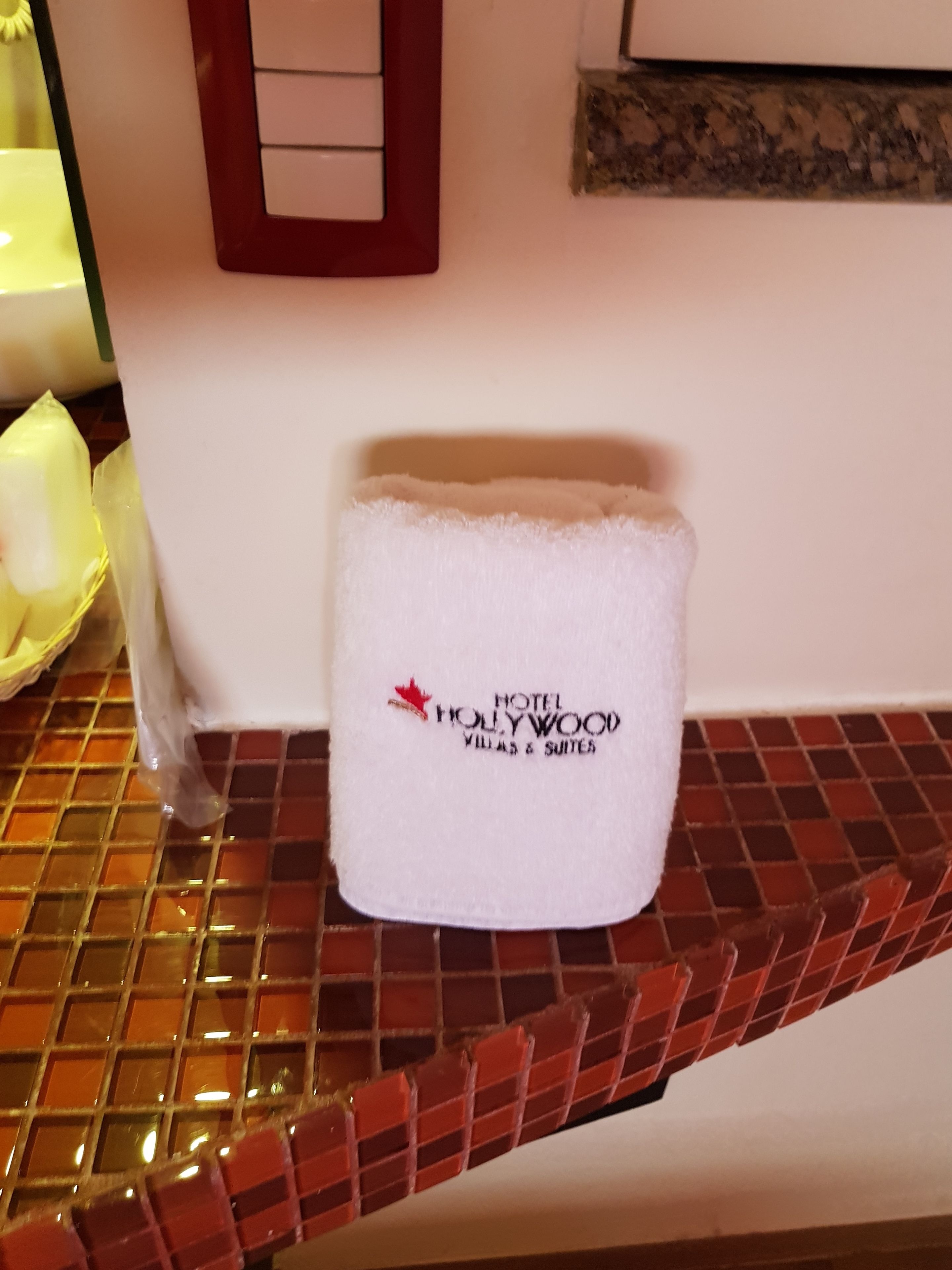 Een witte handdoek met de tekst 'HOTEL HOLLYWOOD VILLAS & SUITES' erop, op een betegeld oppervlak.