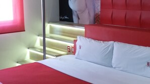 Un dormitorio moderno con una colcha roja, un cartel grande de una mujer en la pared, y una escalera con escalones rojos.