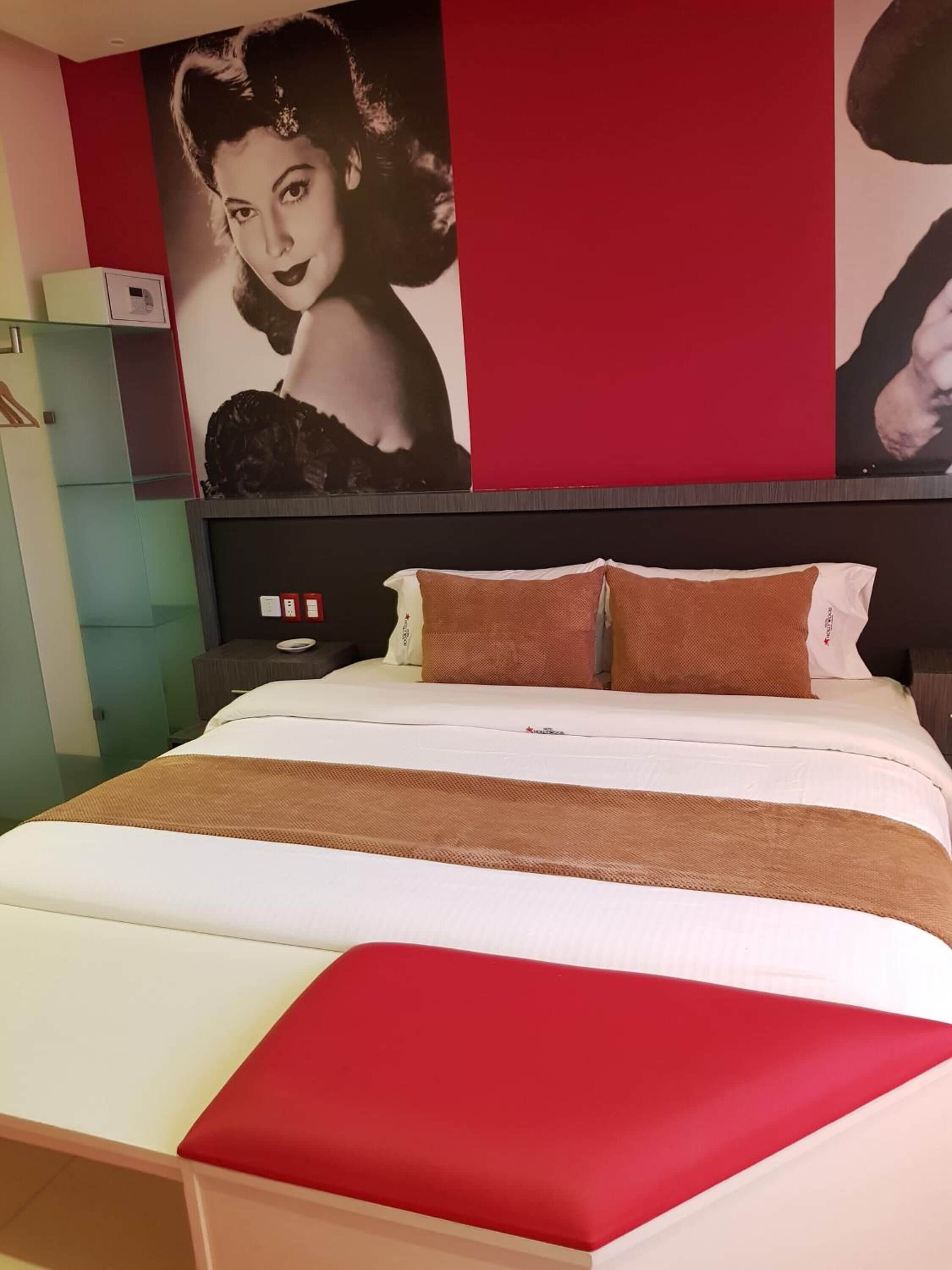 A hotel room with a large bed, red and white bedding, and a wall with a large poster.