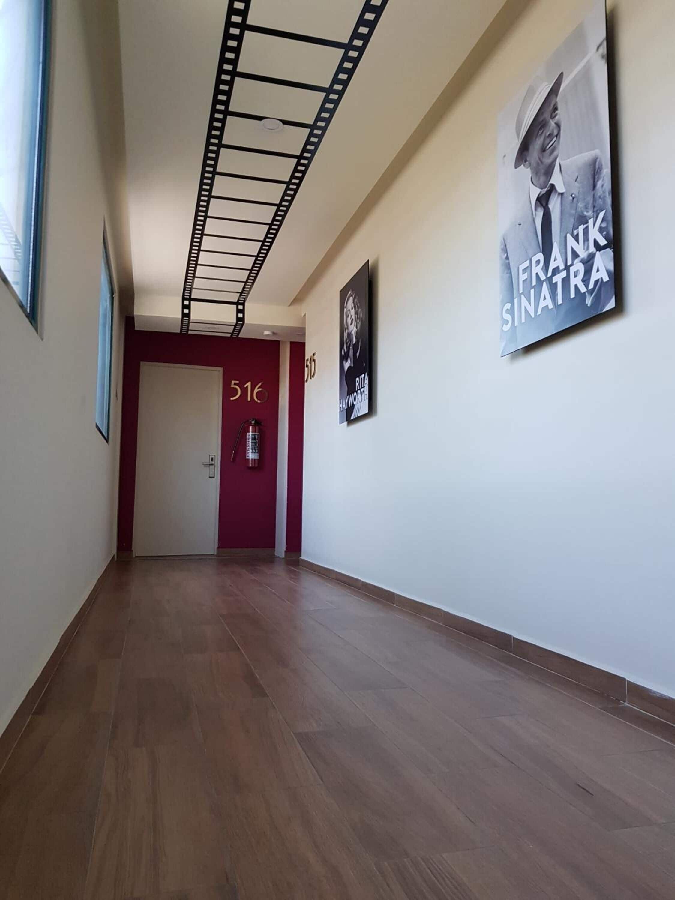 Um corredor com piso de madeira, uma porta vermelha com a inscrição '516' e um extintor de incêndio na parede.