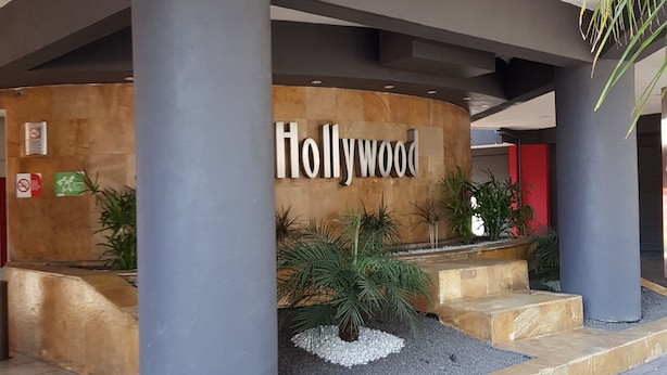 Un edificio con un cartel de 'Hollywood', grandes columnas y una zona ajardinada con plantas y una pequeña fuente.