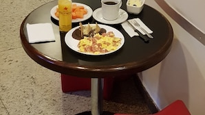 Una pequeña mesa redonda con artículos de desayuno, como un plato de huevos, un vaso de zumo de naranja y una taza de café.