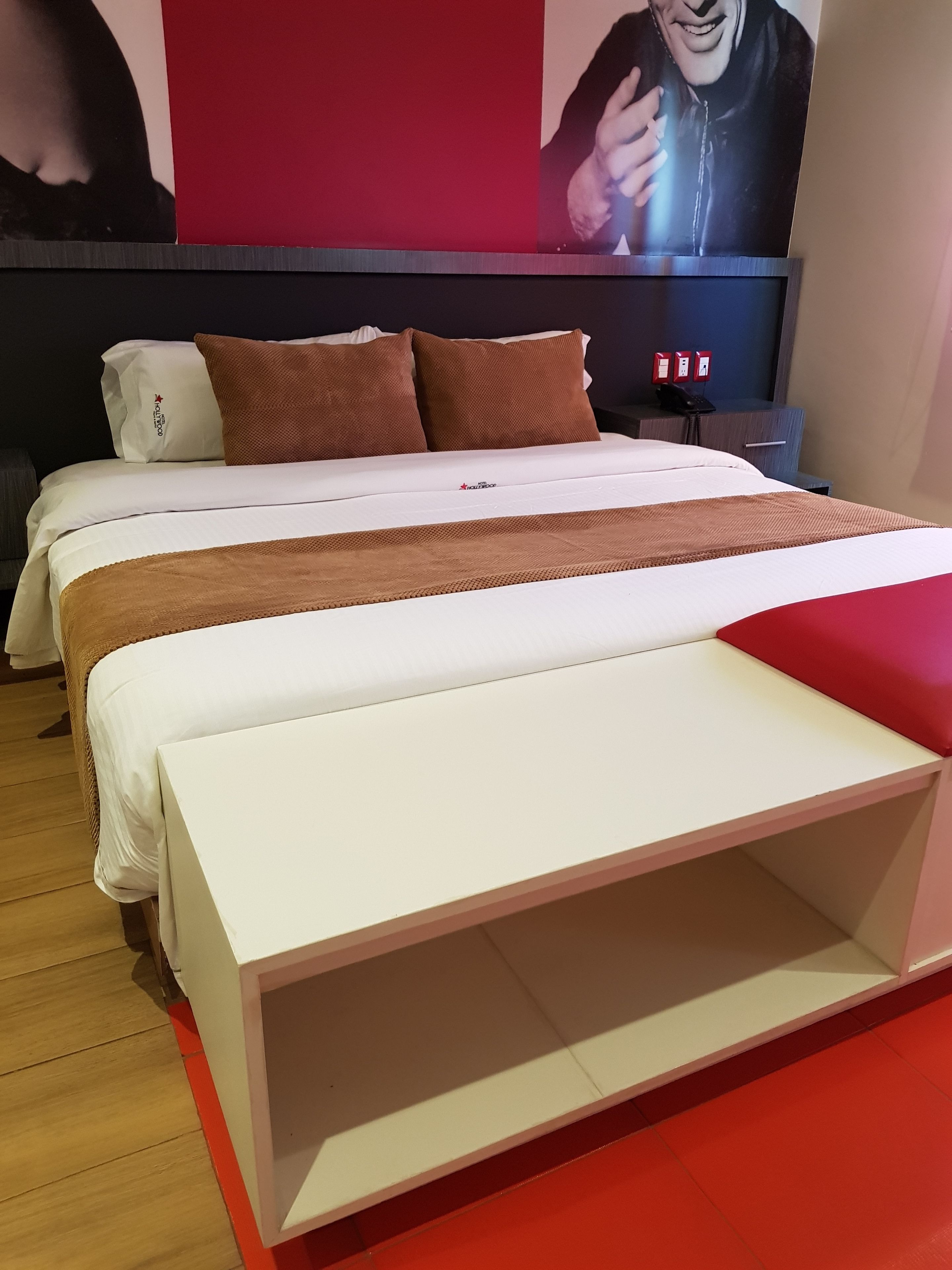 Una habitación de hotel moderna con una cama grande, una pared de acento roja y un banco blanco original.